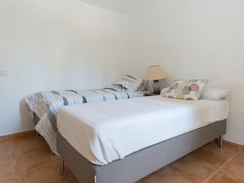 Chambre sobre avec deux lits simples, sol en terre cuite et murs blancs.