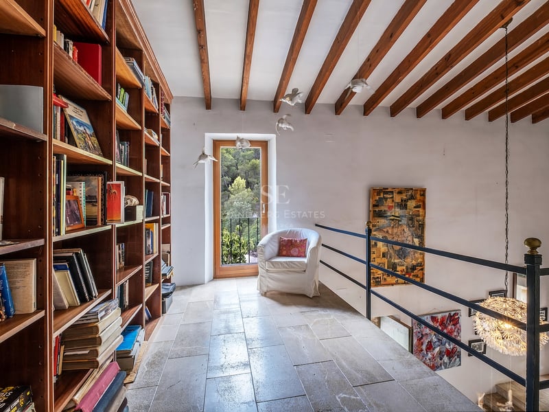 Bibliothèque en mezzanine avec étagères en bois du sol au plafond, sol en pierre et poutres apparentes.