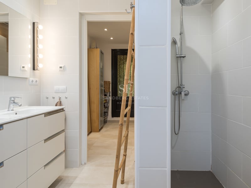 Salle de bain lumineuse avec carrelage blanc, grande douche à l'italienne et double vasque blanche.
