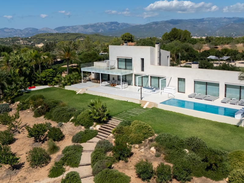 Vue extérieure d'une villa moderne avec piscine à débordement, de grandes baies vitrées et des jardins luxuriants. Architecture minimaliste.