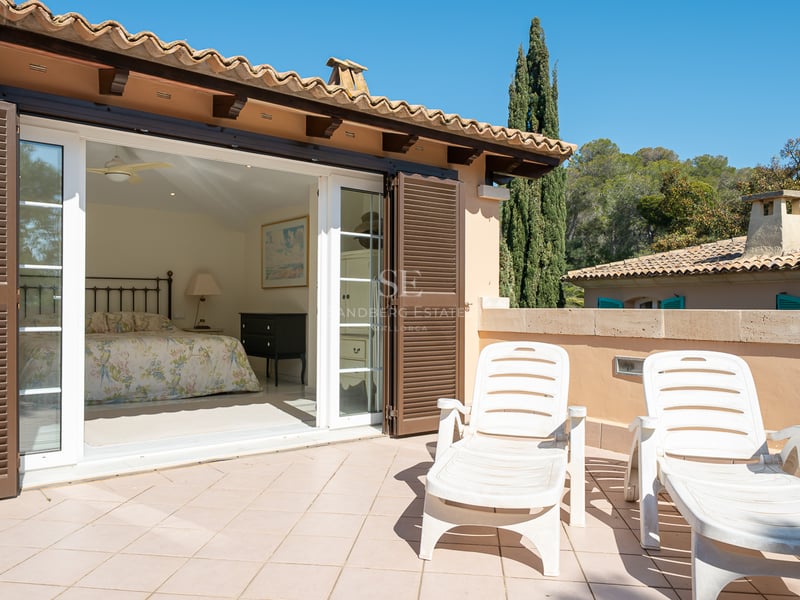 Chambre avec lit en fer forgé s'ouvrant sur une grande terrasse en terre cuite avec deux chaises longues.