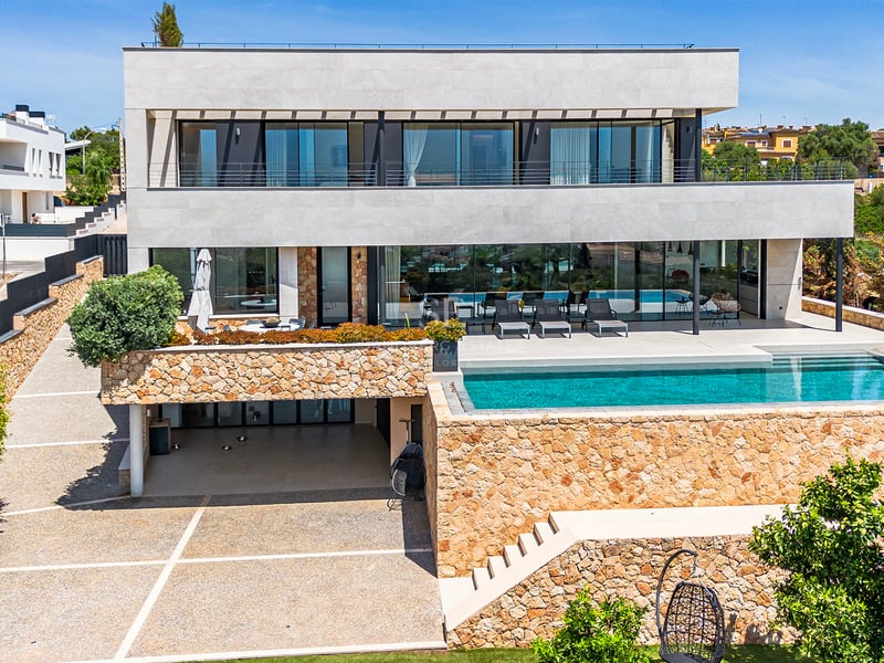 Façade d'une villa contemporaine avec murs en pierre naturelle, grandes baies vitrées et piscine turquoise.