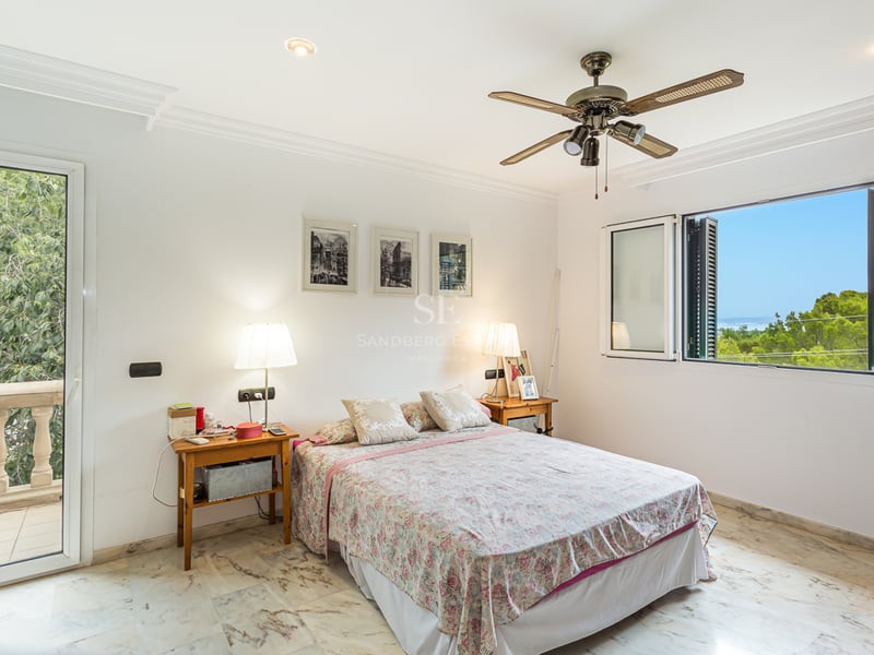 Chambre blanche avec sol en marbre, lit double, ventilateur de plafond et fenêtre offrant une vue sur la mer.