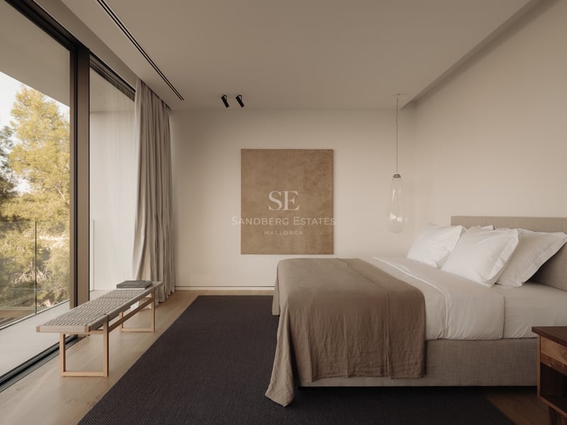 Chambre minimaliste avec baies vitrées, parquet en bois, linge de lit en lin et vue sur la végétation.
