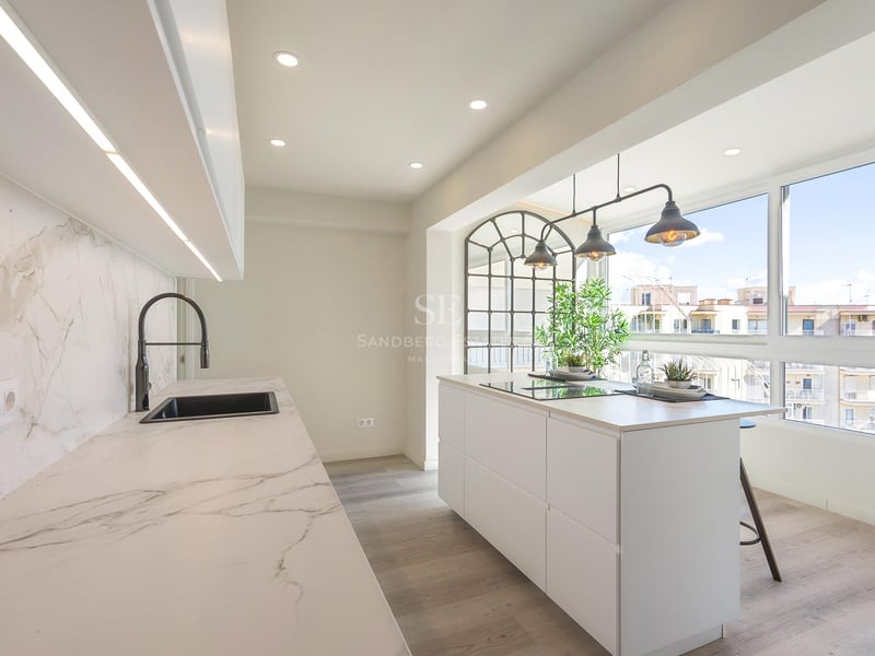 Cuisine blanche contemporaine avec îlot en marbre, suspensions industrielles et grandes fenêtres vue ville.