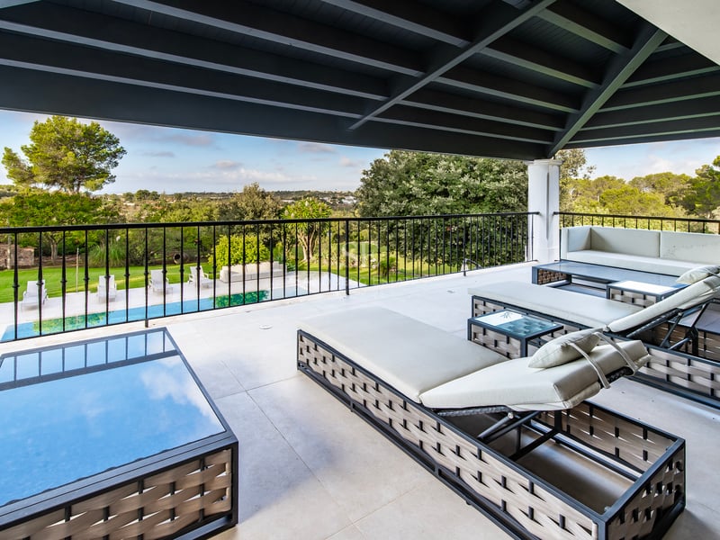Terrasse couverte avec bains de soleil gris et garde-corps noir dominant un jardin verdoyant et une piscine.