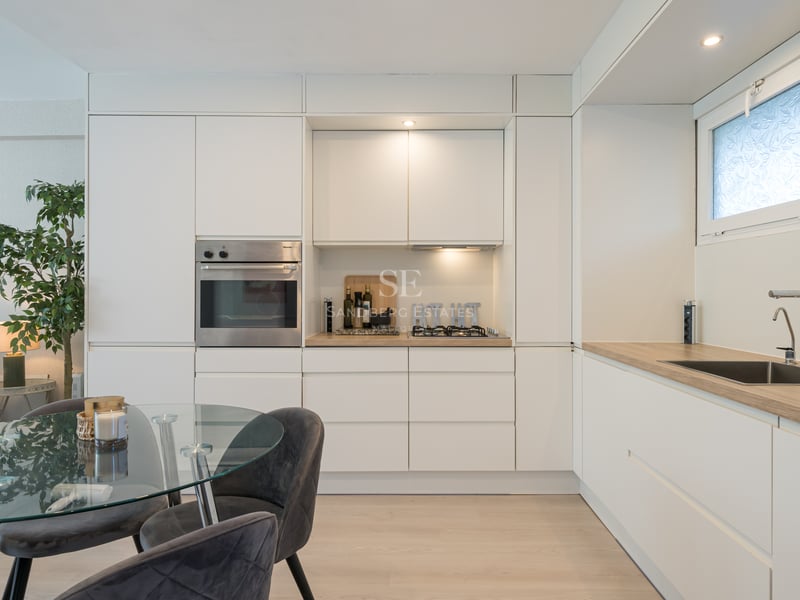 Cuisine minimaliste blanche avec four Miele, plan de travail effet bois et table à manger en verre.