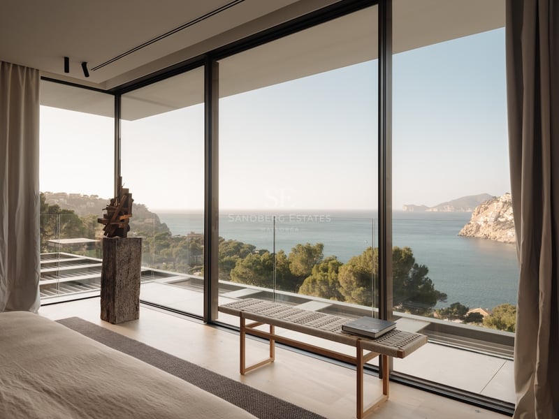Chambre moderne dotée de baies vitrées toute hauteur offrant une vue sur une baie turquoise et des falaises.