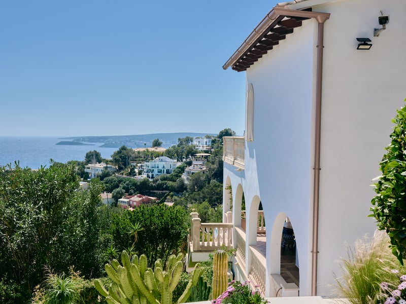 Vue latérale d'une villa blanche avec terrasses à arcades surplombant la côte et la mer Méditerranée.