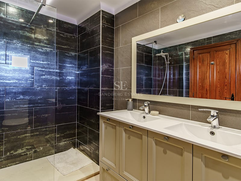 Salle de bains moderne avec double vasque, grand miroir et douche vitrée avec carrelage mural sombre texturé.