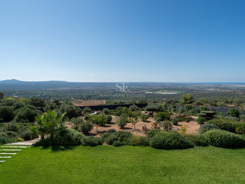 Vue de piscine à débordement avec transats et jardin luxuriant. Architecture moderne avec larges baies vitrées et ciel dégagé.