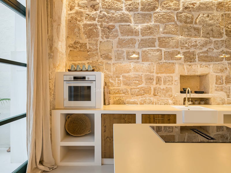 Cuisine moderne avec mur en pierre rustique, comptoirs blancs, accents en bois et îlot avec plaque de cuisson.