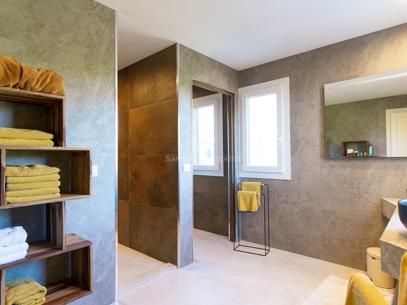 Salle de bain élégante avec murs en pierre grise, étagères en bois avec serviettes jaunes et vasques noires.