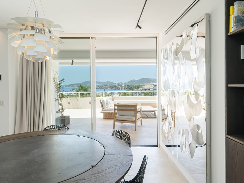 Salle à manger de luxe avec table ronde, suspension design et baies vitrées donnant sur une baie méditerranéenne.