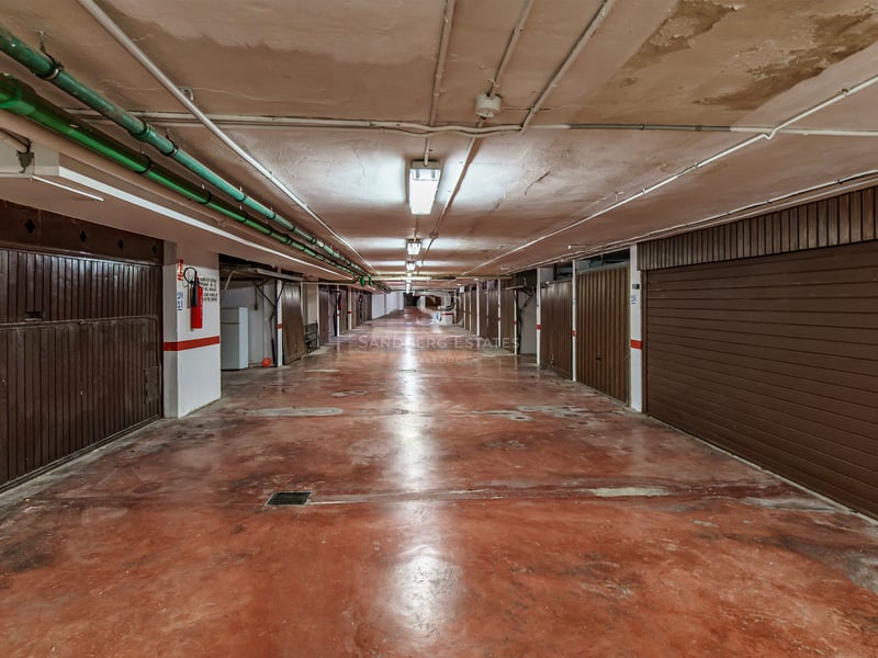 Couloir de parking souterrain avec sol rouge et portes de garage individuelles marron des deux côtés.