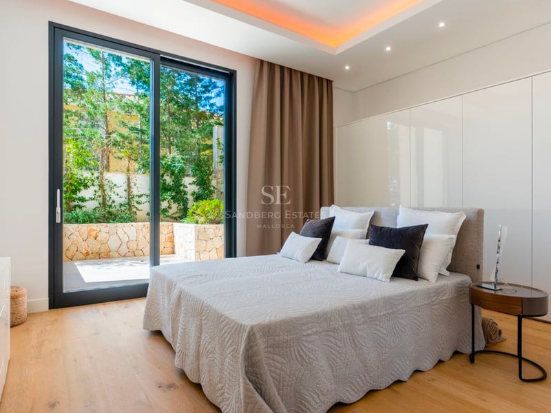 Chambre lumineuse avec grand lit, parquet en bois et baie vitrée coulissante donnant sur un patio privé verdoyant.