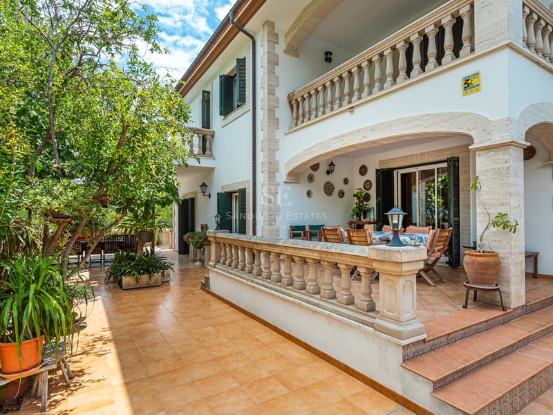 Terrasse en terre cuite avec balustrades en pierre, table à manger ombragée et arbres verdoyants.