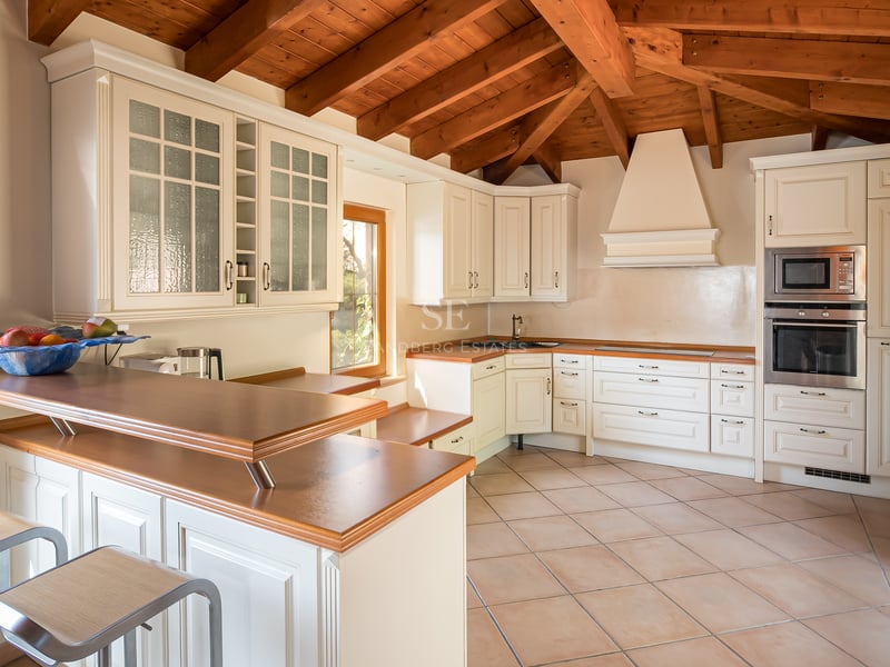 Cuisine rustique avec placards blancs, plans de travail en bois et poutres en bois massif au plafond.