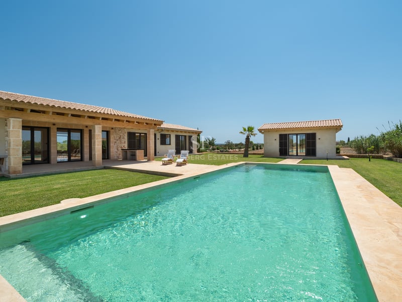 Gran piscina turquesa con terraza de piedra natural y villa de estilo mediterráneo bajo un cielo azul despejado.