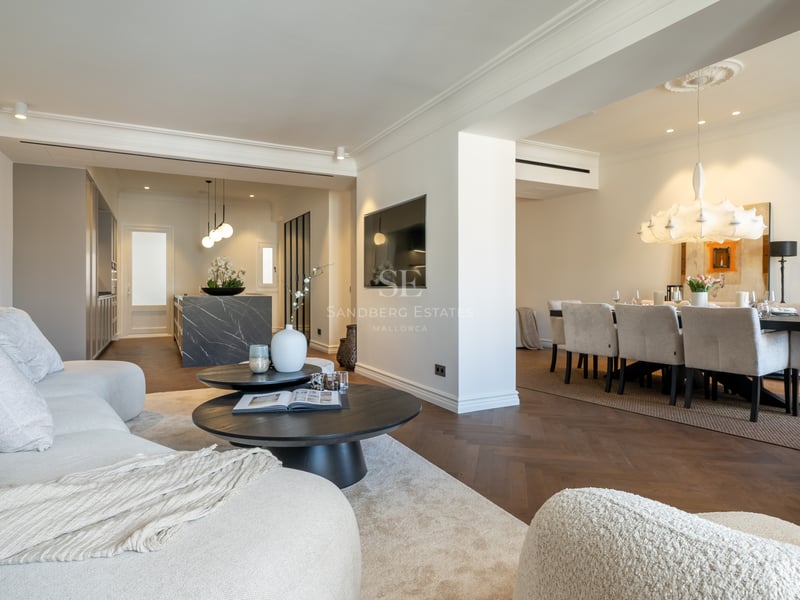 Contemporary open-plan living room with herringbone wood floors, white boucle sofas, and dark marble kitchen island.