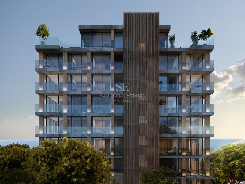 Immeuble moderne de plusieurs étages avec balcons en verre et accents de bois, entouré d'arbres et vue sur la mer.