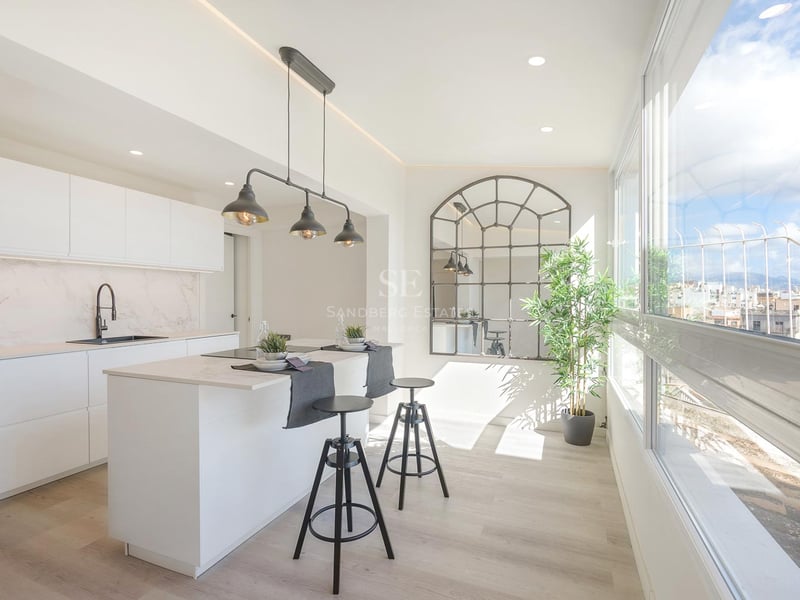 Cuisine moderne lumineuse avec îlot blanc, tabourets industriels noirs et grandes fenêtres donnant sur la ville.