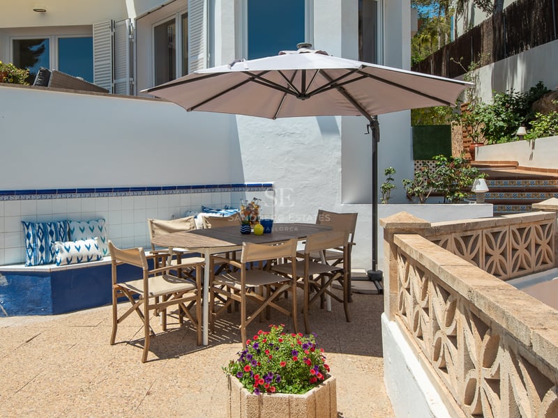 Terrasse ensoleillée avec table en bois, parasol, banc en carreaux bleus et balustrade en pierre sculptée.