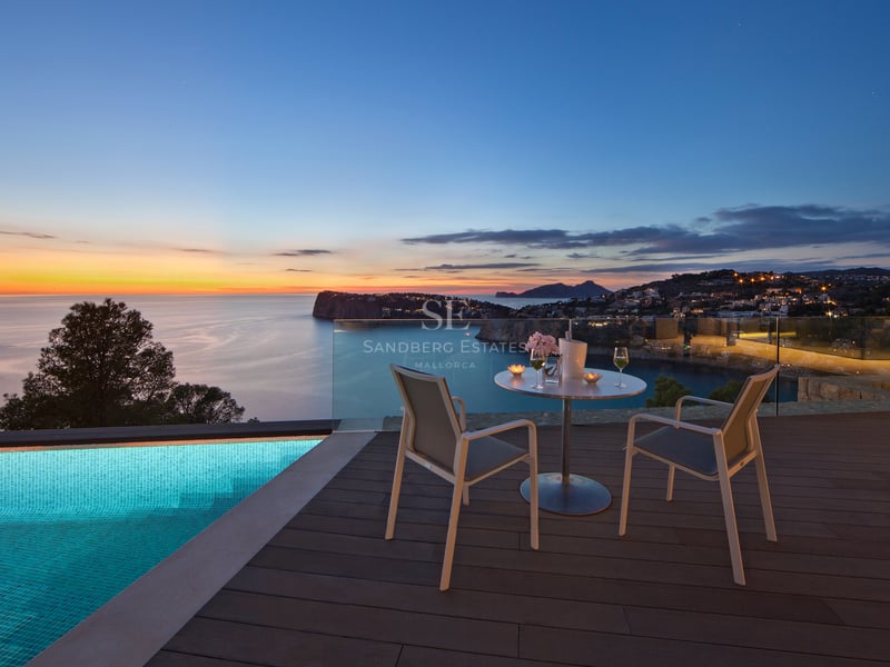 Terrasse de luxe avec piscine à débordement, table pour deux et vue panoramique sur la mer au coucher du soleil.