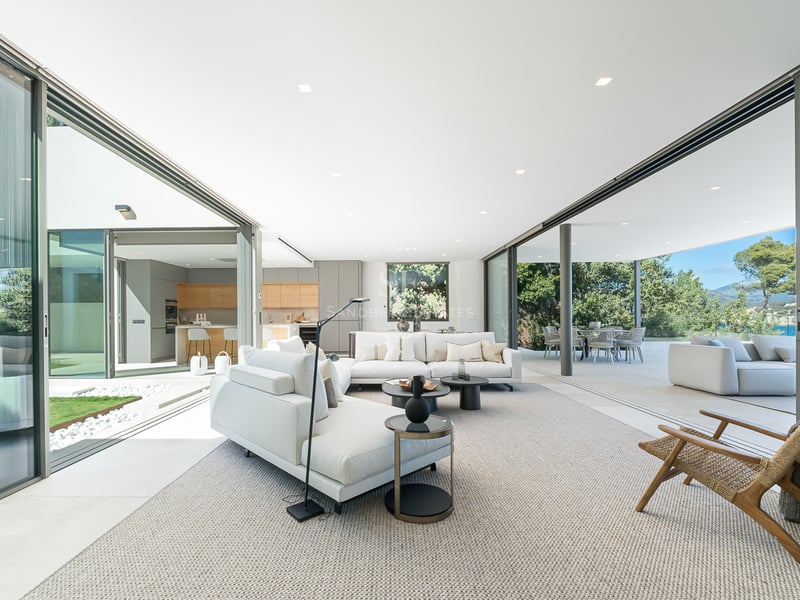 Salon moderne et lumineux avec de grandes baies vitrées ouvrant sur le jardin, comprenant des canapés blancs.