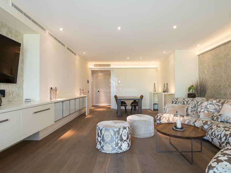 Salon moderne avec canapé à motifs, parquet en bois sombre et meuble TV intégré sous un éclairage chaleureux.