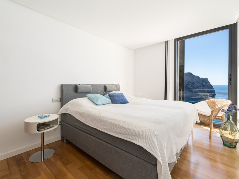 Chambre contemporaine avec lit gris, parquet en bois et baie vitrée offrant une vue sur la mer et les falaises.