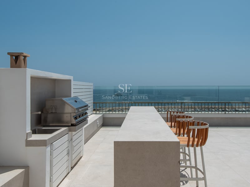 Terrasse moderne sur le toit avec cuisine d'été, bar en béton et tabourets en bois surplombant la mer et le port.