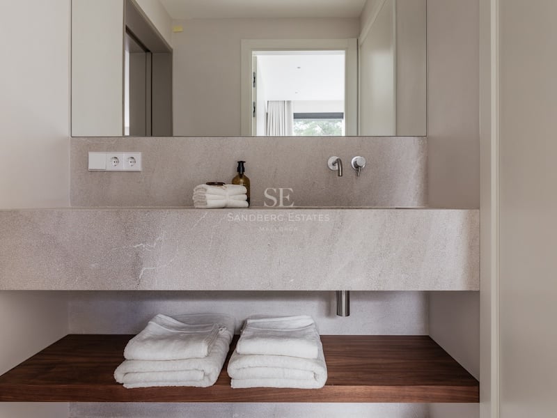 Lavabo minimaliste en pierre avec robinets muraux, étagère en bois et serviettes blanches.