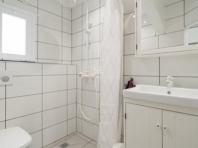 Salle de bain carrelée en blanc avec lavabo, toilettes et coin douche avec rideau blanc.