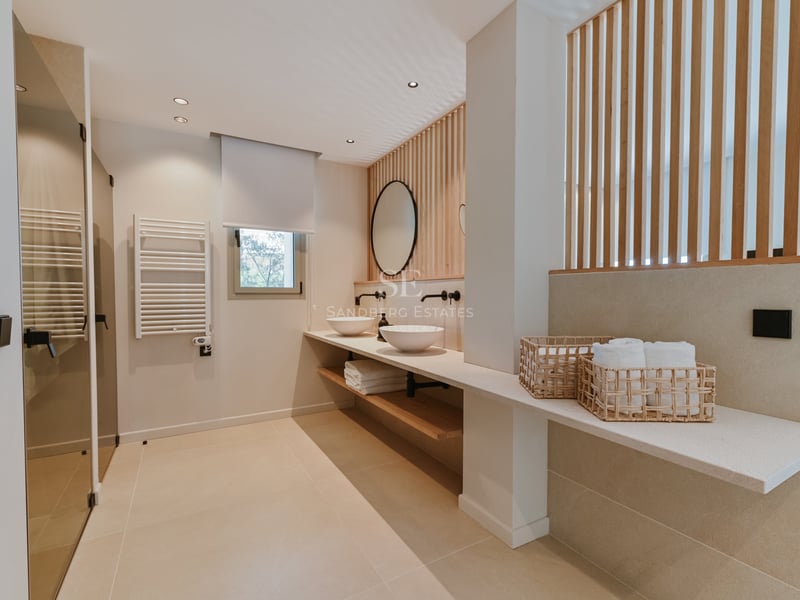 Salle de bain contemporaine avec meuble double vasque, mur en lattes de bois et miroir circulaire.
