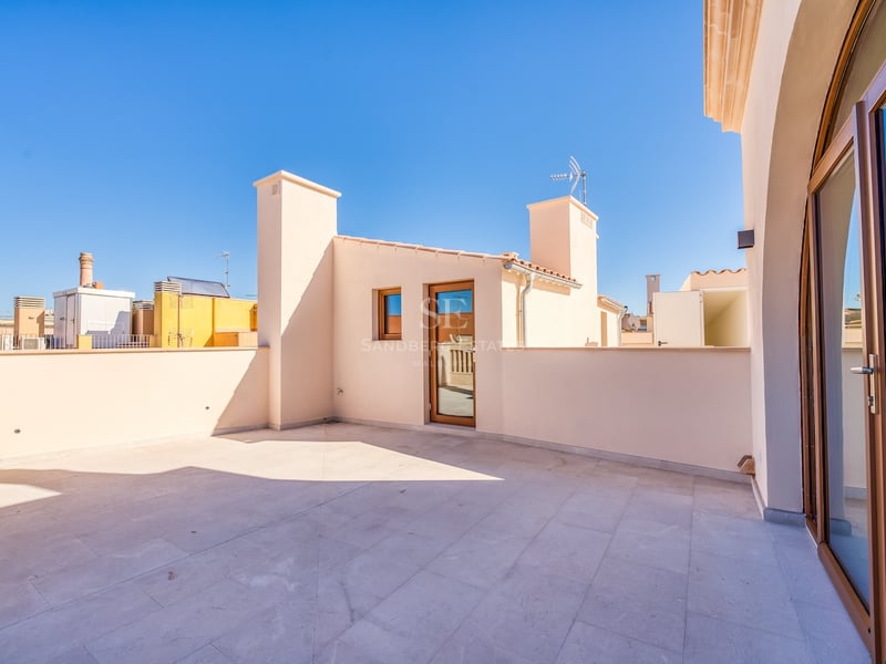 Large rooftop terrace with natural stone tiling and cream walls under a clear blue sky.