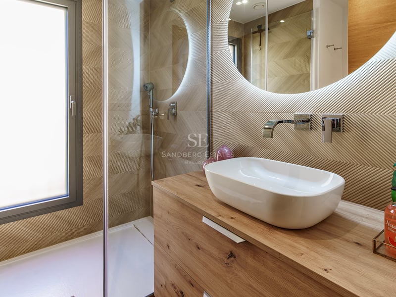 Salle de bain avec vasque à poser sur bois, miroir rond rétroéclairé et paroi de douche en verre.