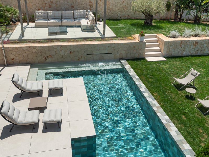 Vue d'en haut d'une piscine turquoise, chaises longues de designer sur patio et pelouse impeccable.