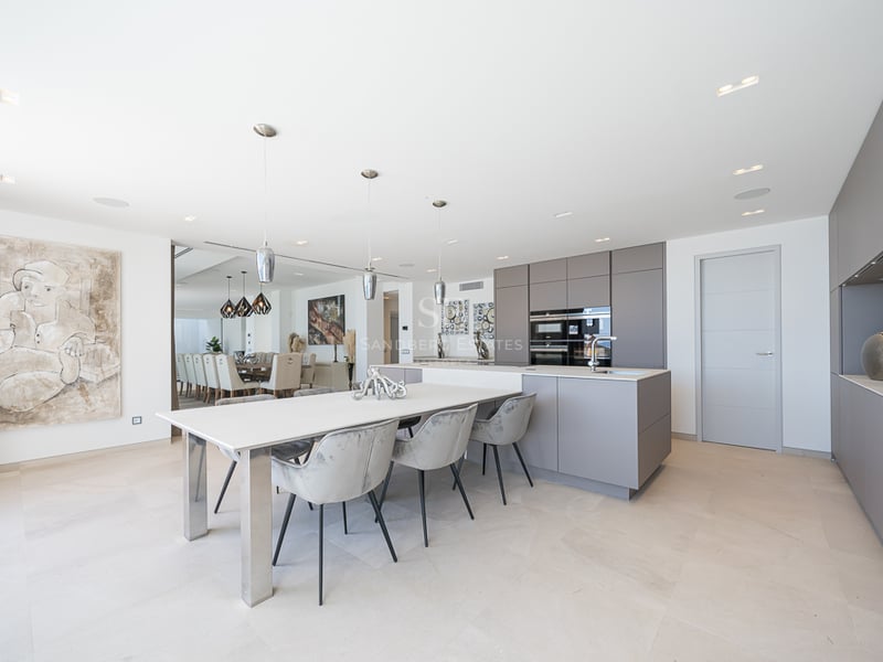 Cuisine moderne avec placards gris, îlot blanc avec table à manger et chaises en velours gris.