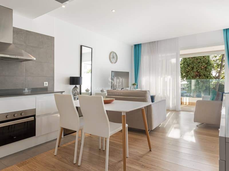 Pièce à vivre lumineuse avec cuisine ouverte, salle à manger et accès à un balcon verdoyant.