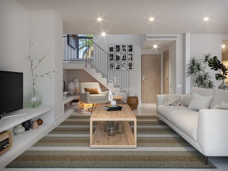 Salon lumineux avec canapé blanc, table basse en bois, tapis rayé et un escalier moderne en arrière-plan.