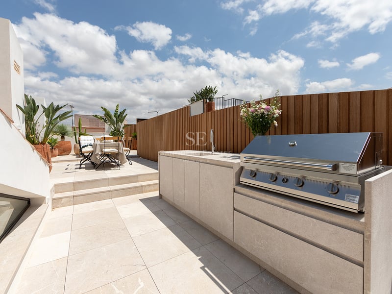 Terraza contemporánea con cocina exterior de piedra, barbacoa integrada, valla de madera y zona de comedor al aire libre.