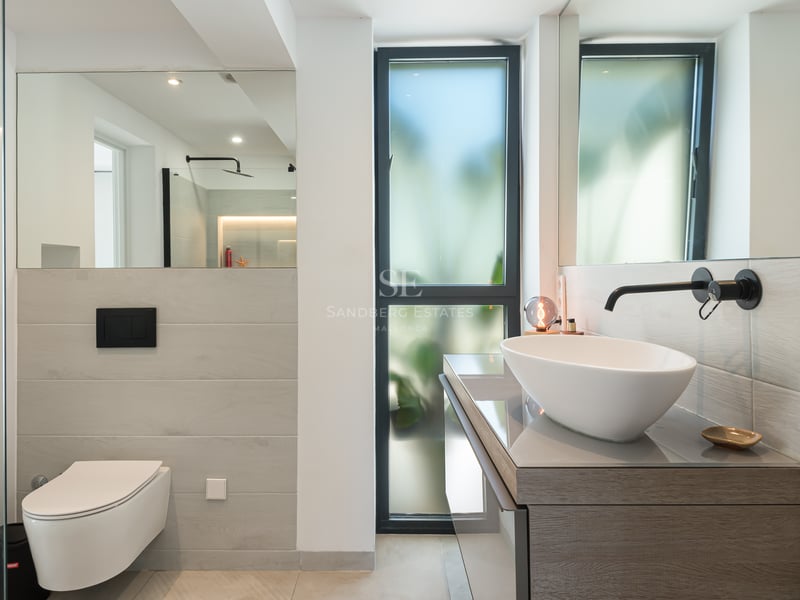 Salle de bain contemporaine avec vasque à poser blanche, robinetterie noir mat, WC suspendu et grands miroirs.