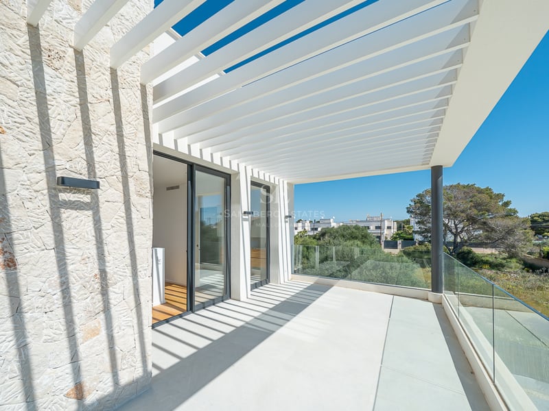 Terrasse ensoleillée avec pergola à lames blanches projetant des ombres sur un mur en pierre et garde-corps en verre.