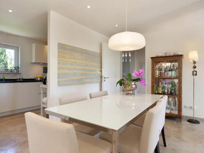 Salle à manger contemporaine avec sol en marbre, table blanche et chaises crème à côté d'une cuisine moderne.