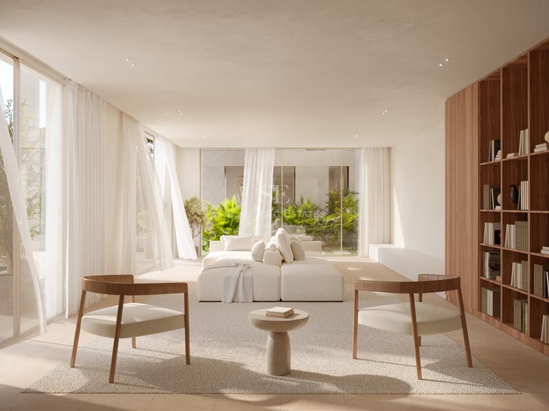 Salon lumineux avec canapé modulaire blanc, deux fauteuils en bois et baies vitrées donnant sur un jardin verdoyant.