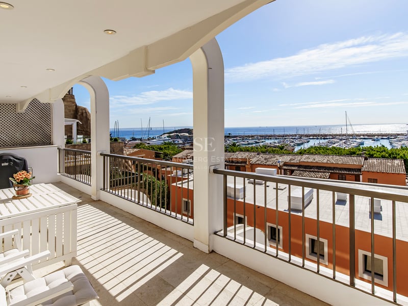 Balcon blanc avec arches et mobilier d'extérieur offrant une vue sur un port de plaisance et la mer bleue.