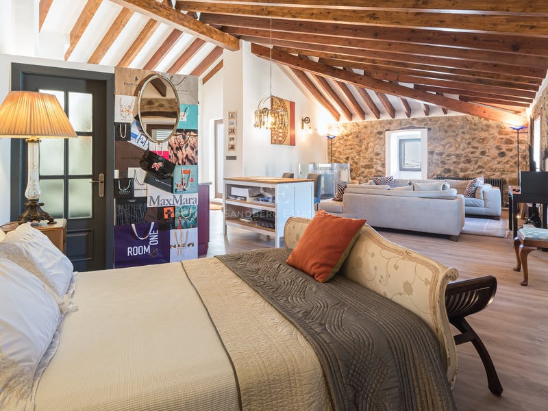 Chambre de luxe avec poutres en bois apparentes, murs en pierre naturelle et coin salon intégré.