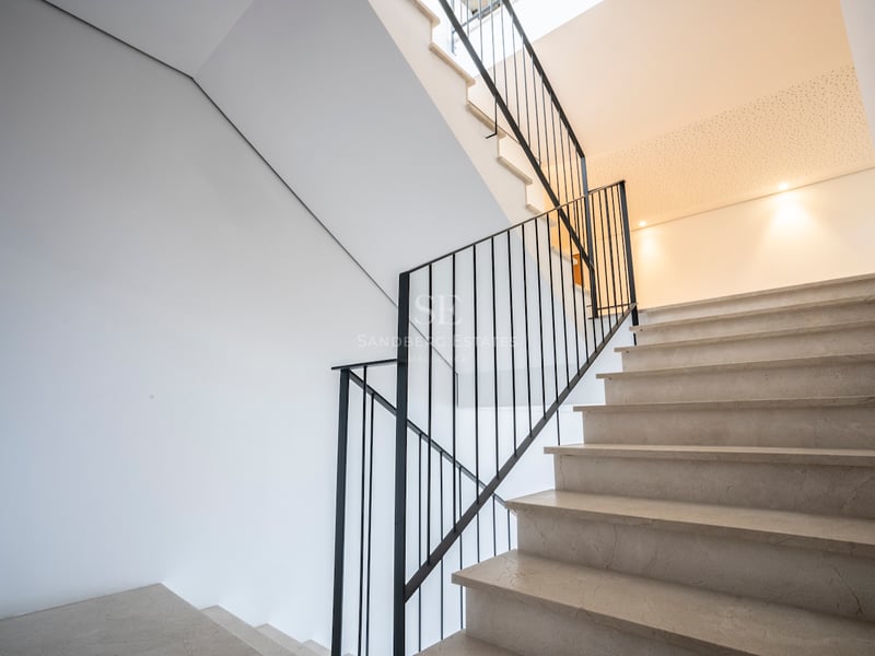 Escalier en marbre crème avec rampe en fer noir contre des murs blancs sous une lumière naturelle douce.