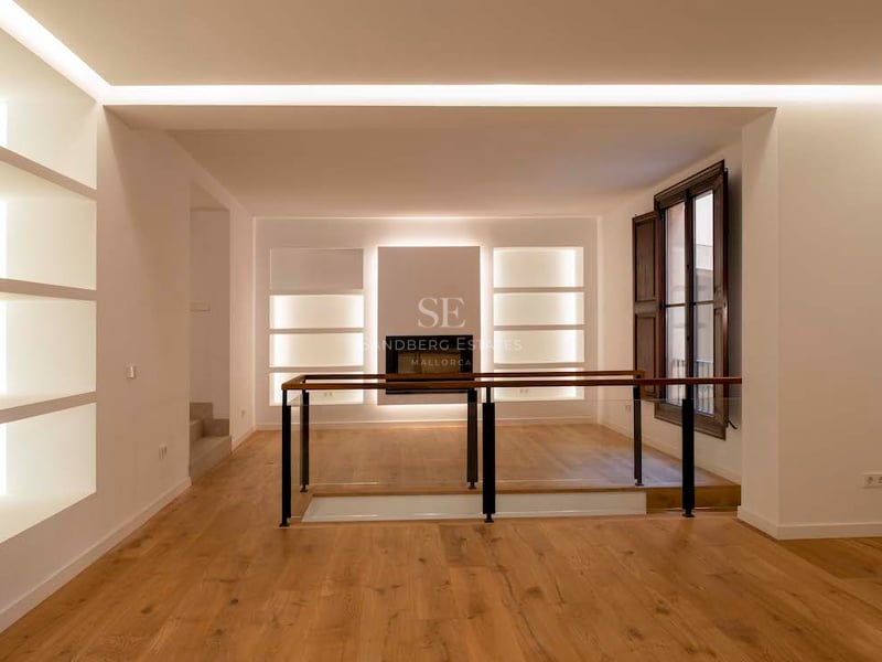 Intérieur minimaliste avec parquet en chêne, murs blancs avec niches éclairées et garde-corps en verre.